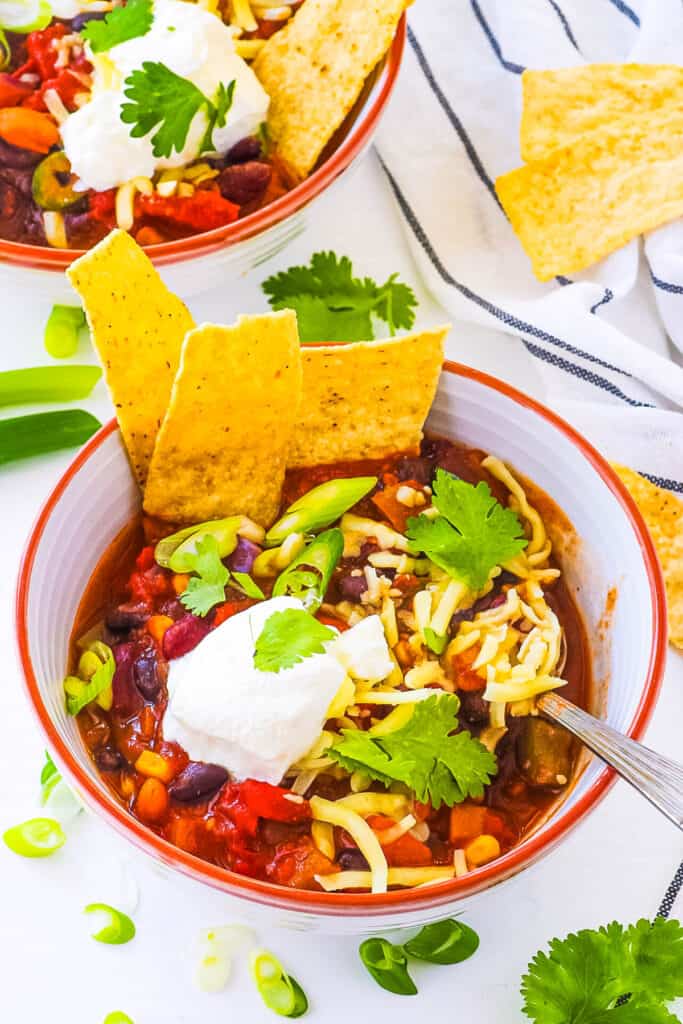 The best Instant Pot vegetarian chili, served in a bowl garnished with green onions, cheese, sour cream and tortilla chips.
