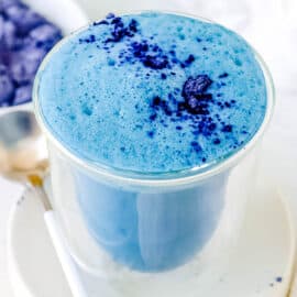 Blue latte served in a glass with a garnish of butterfly pea flower powder on top.