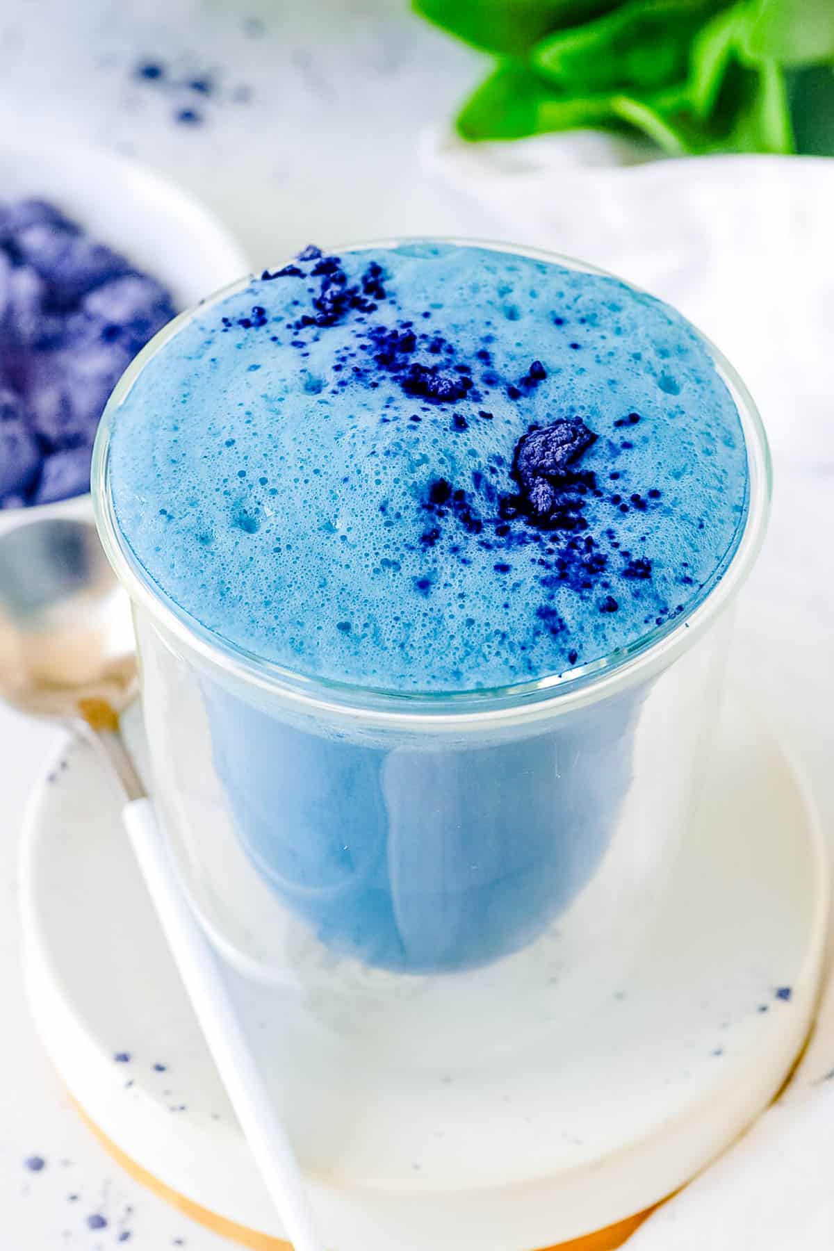 Blue latte served in a glass with a garnish of butterfly pea flower powder on top.