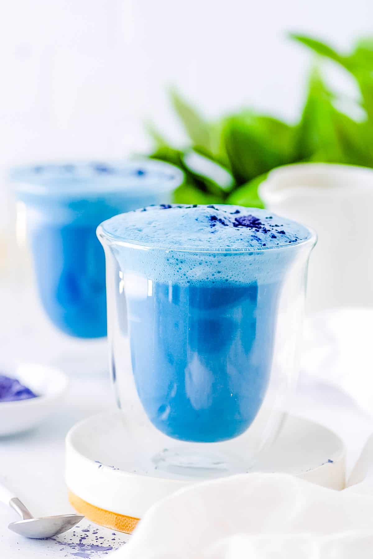Blue latte served in a glass with a garnish of butterfly pea flower powder on top.