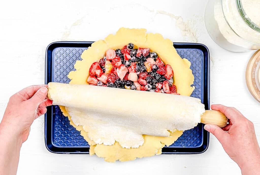 Pie crust being added to the top of the fruit pie in a baking dish.