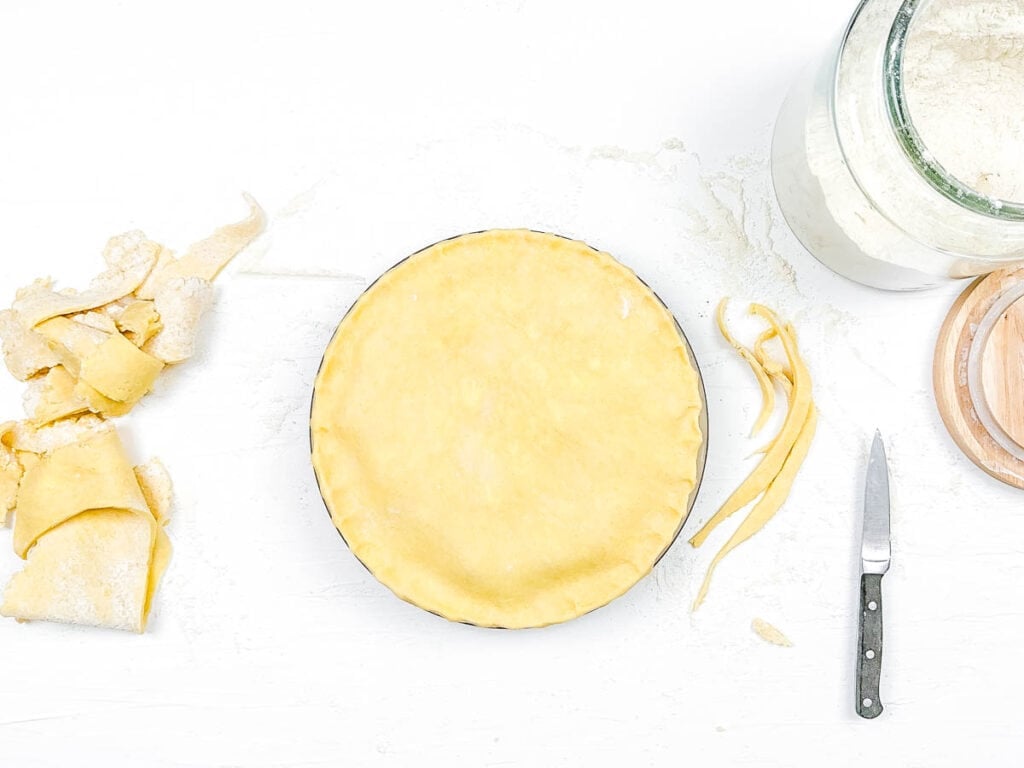 Pie crust being trimmed along the edges of a baking dish.