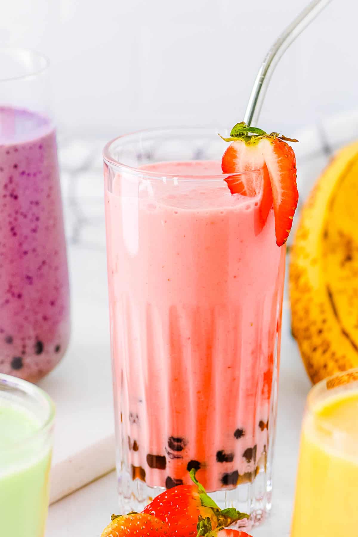 Boba smoothie with four different flavors (strawberry banana, mango, honeydew, and blueberry) served on a white countertop.