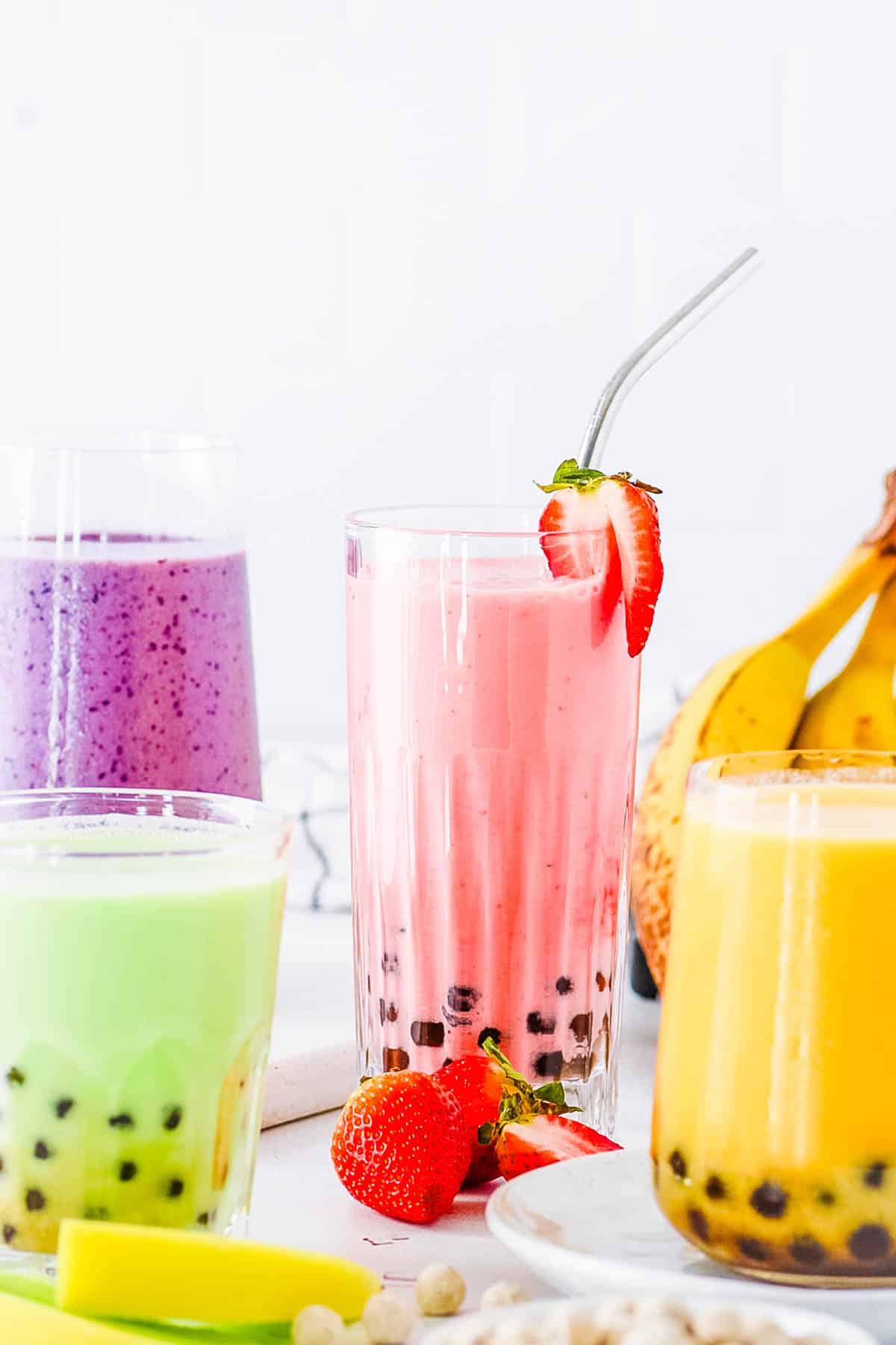 Boba smoothie with four different flavors (strawberry banana, mango, honeydew, and blueberry) served on a white countertop.