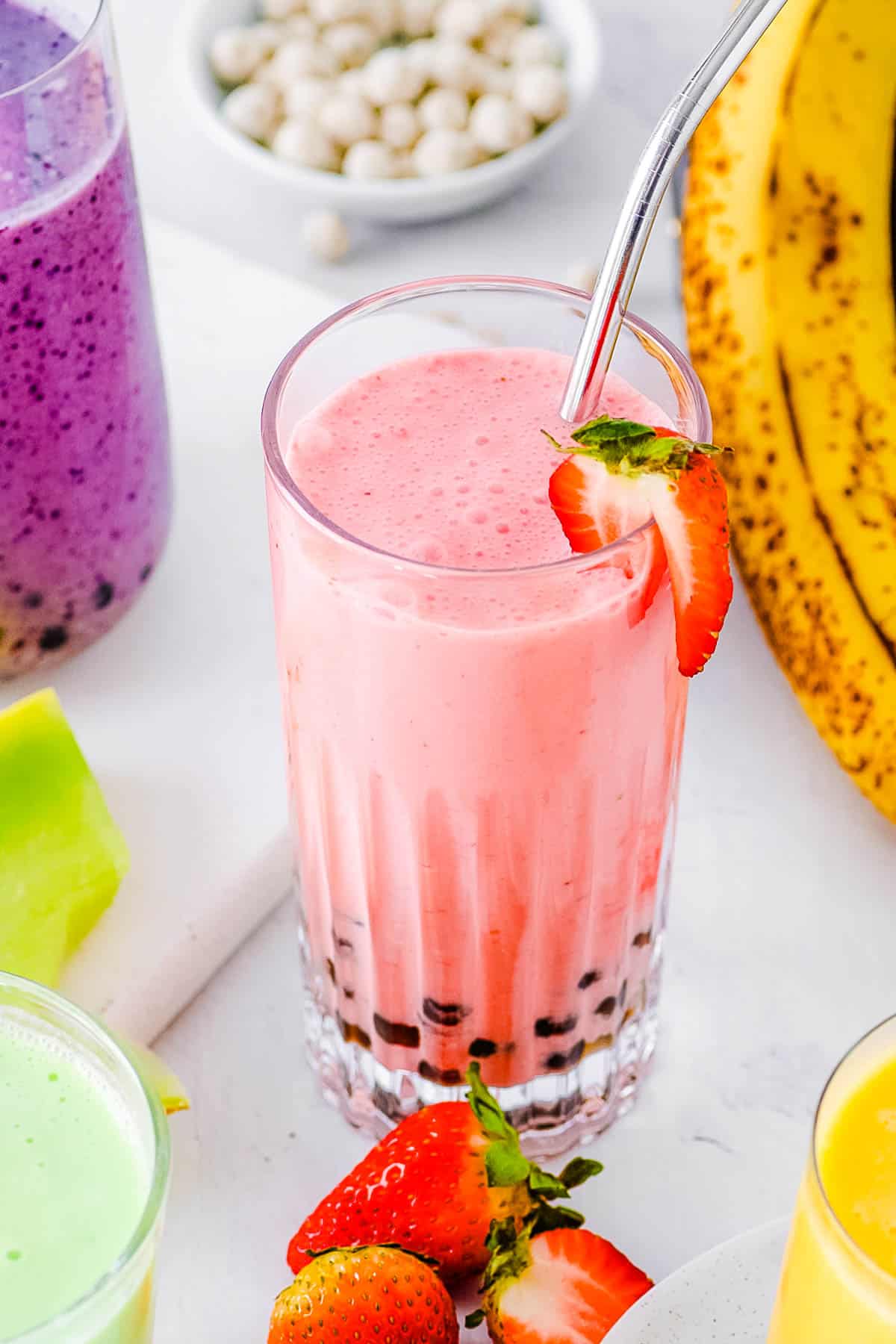 Boba smoothie with four different flavors (strawberry banana, mango, honeydew, and blueberry) served on a white countertop.