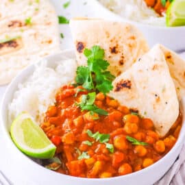 Chickpea tikka masala, served in a white bowl with naan and rice on the side, garnished with cilantro and lime.