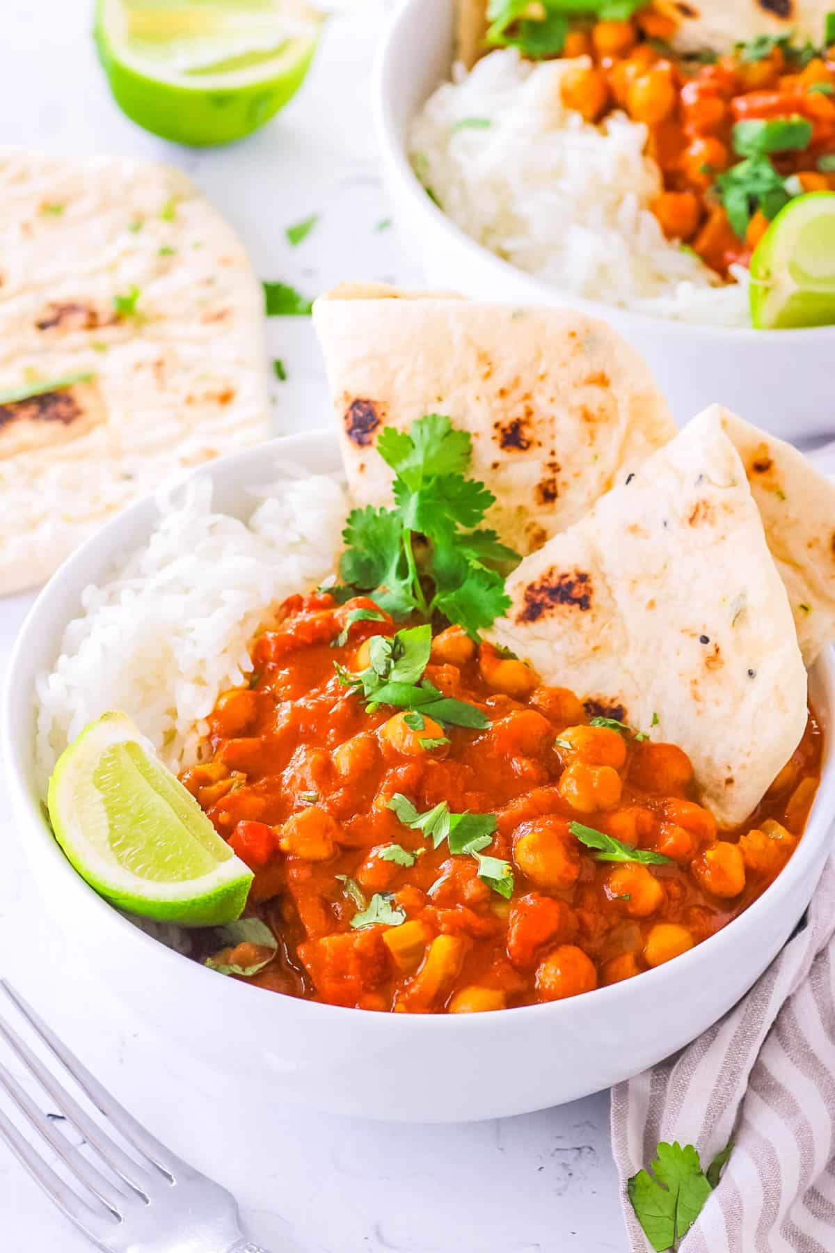 Chickpea tikka masala, served in a white bowl with naan and rice on the side, garnished with cilantro and lime.