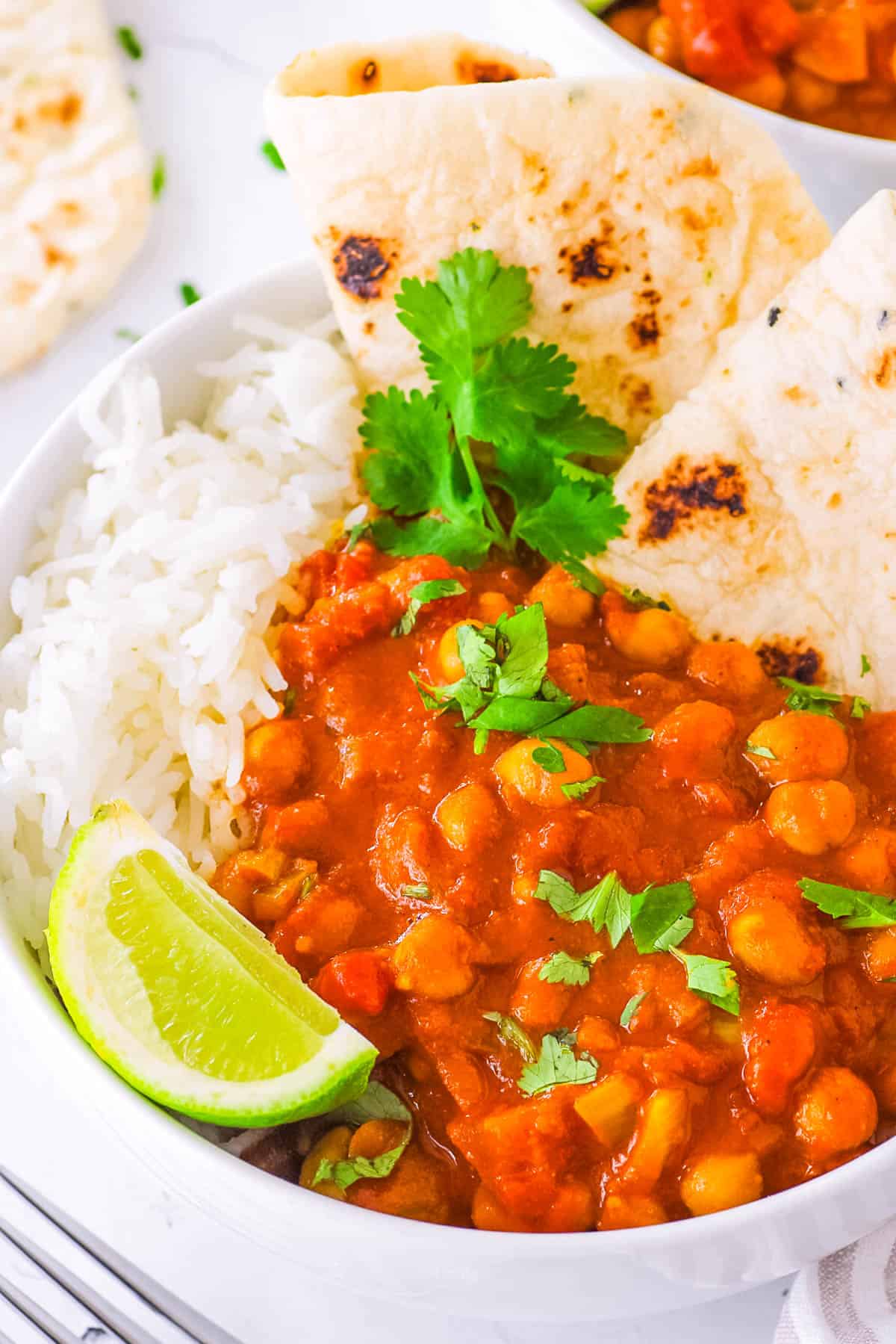 Vegan chickpea tikka masala, served in a white bowl with naan and rice on the side, garnished with cilantro and lime.