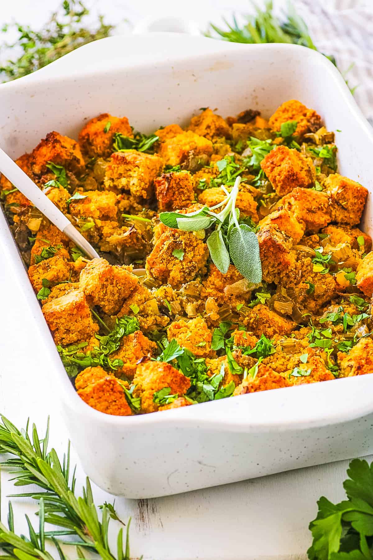 Cornbread gluten free stuffing, served in a white casserole dish, garnished with fresh herbs.