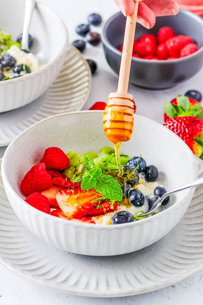 Cottage cheese and fruit bowl with fresh berries and kiwi, with a drizzle of honey on top.