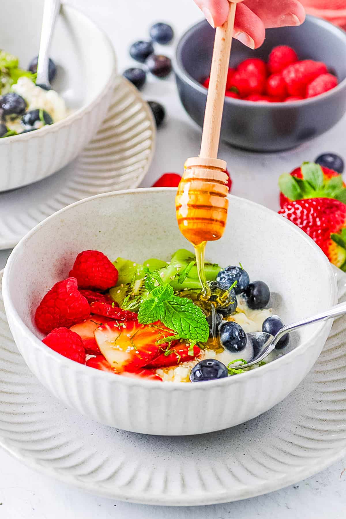 Cottage cheese and fruit bowl with fresh berries and kiwi, with a drizzle of ،ney on top.