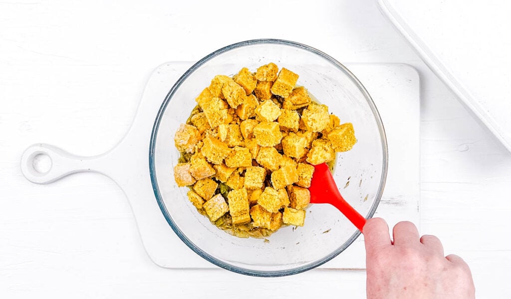 Cornbread cubes mixed with stuffing ingredients in a mixing bowl.