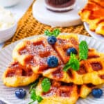 Easy croffles stacked on a white plate, topped with powdered sugar, garnished with blueberries and mint.