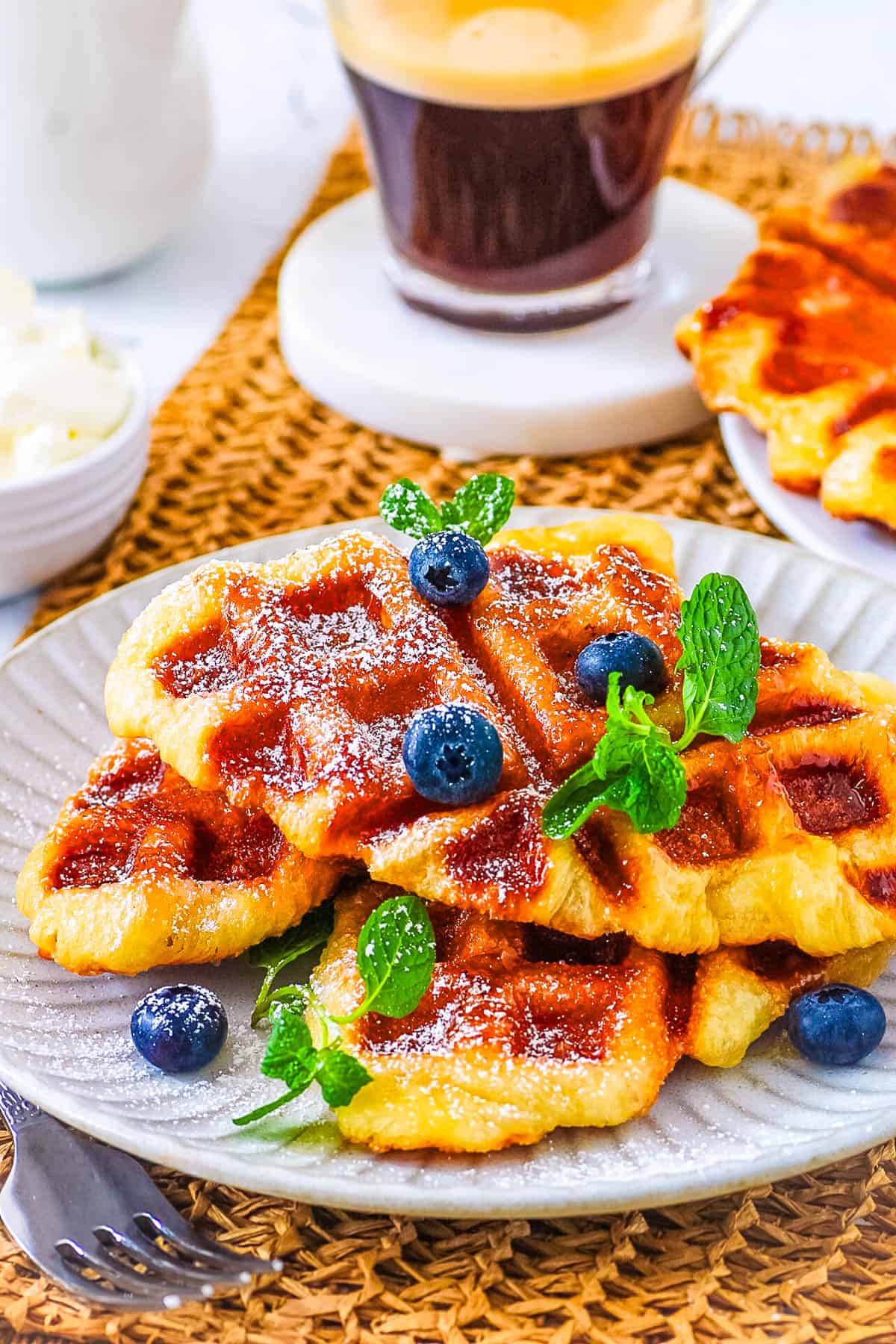 Easy croffles stacked on a white plate, topped with powdered sugar, garnished with blueberries and mint.