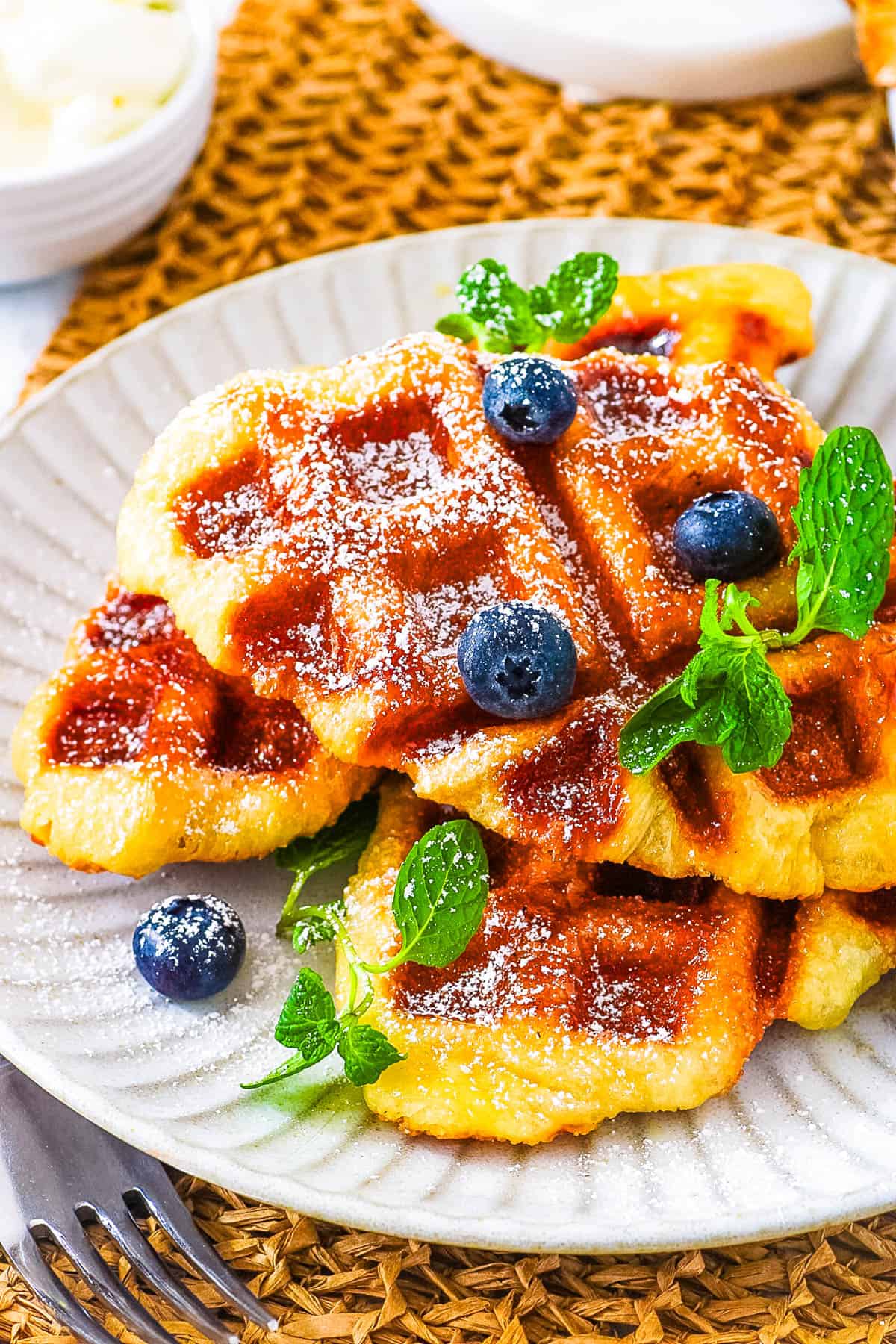Easy croffle recipe stacked on a white plate, topped with powdered sugar, garnished with blueberries and mint.
