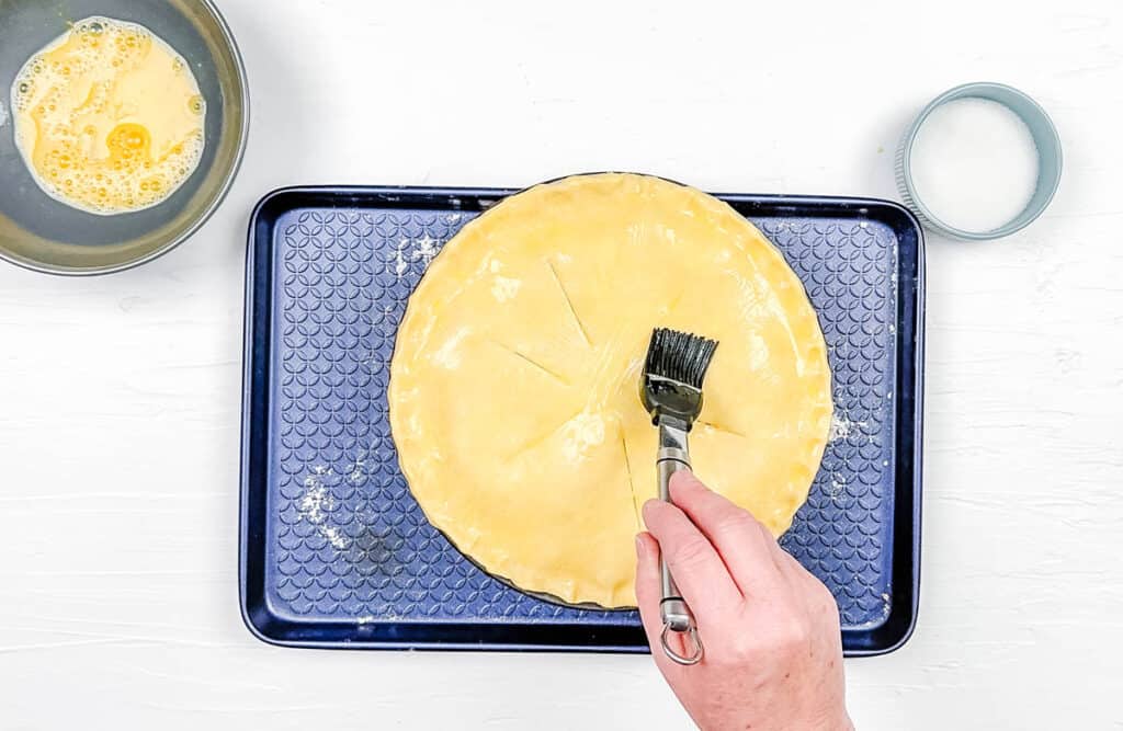 Egg wash being brushed on top of the pie before baking in the oven.