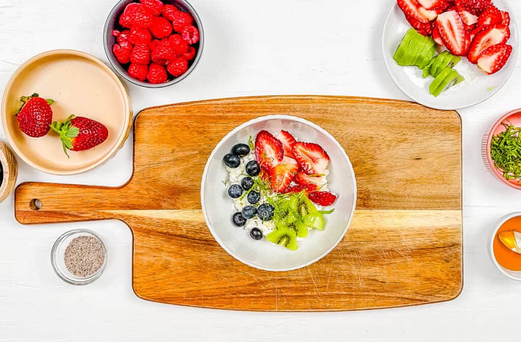 Fruit and cottage cheese served in a white bowl on a cutting board.