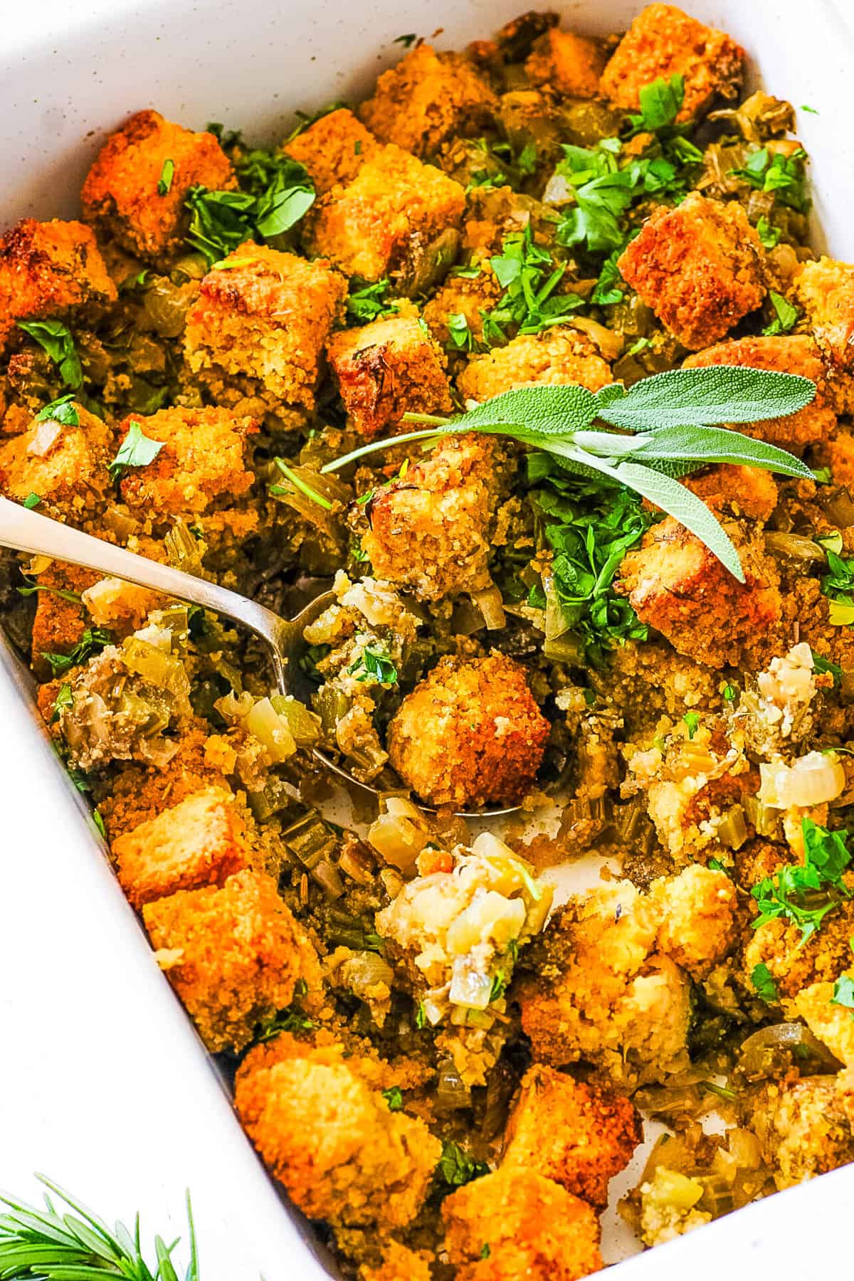 Cornbread gluten free stuffing, served in a white casserole dish, garnished with fresh herbs.