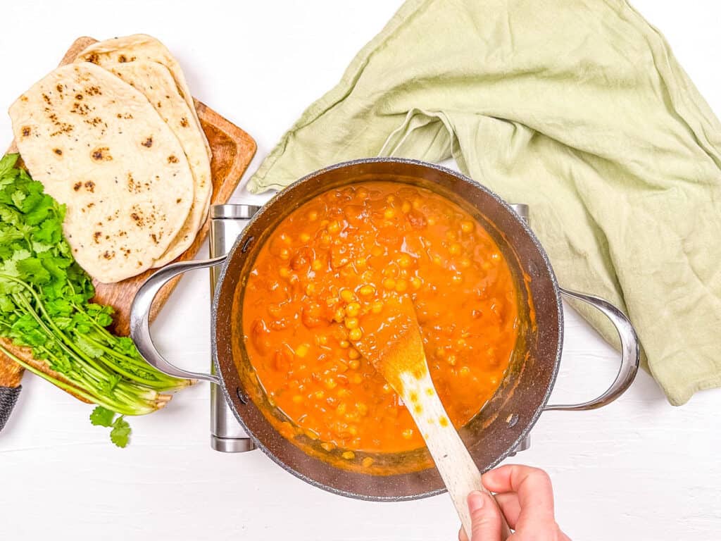 Tomatoes and coconut milk added to chickpeas and spices in a large pot on the stove.