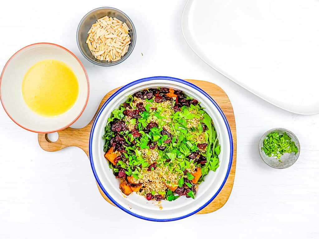 Arugula, quinoa, cranberries and roasted pumpkin combined in a mixing bowl.