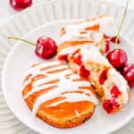 Glazed cherry fritters on a white plate with fresh cherries surrounding them.