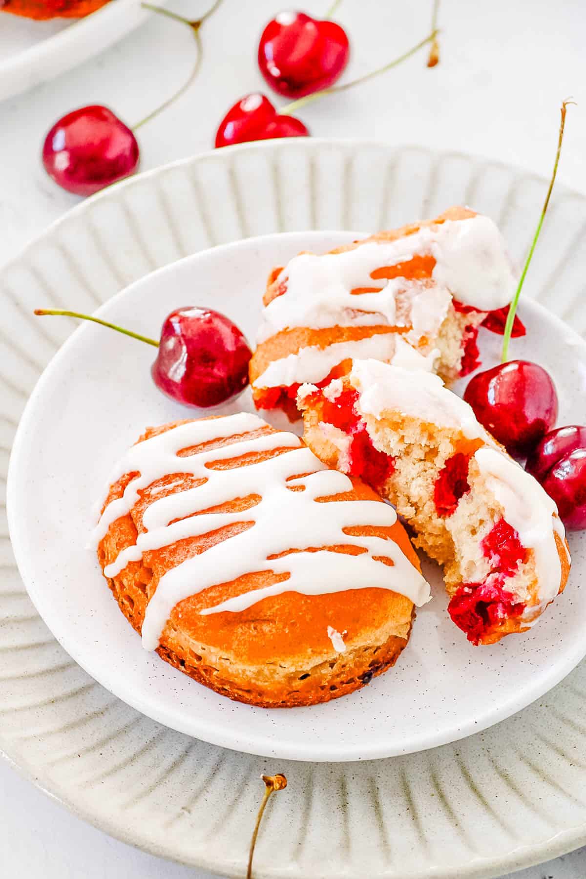 Glazed cherry fritters on a white plate with fresh cherries surrounding them.