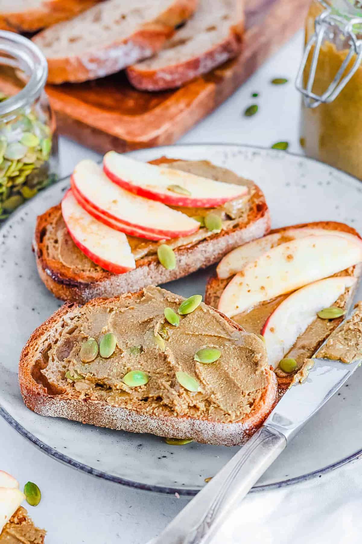 Healthy homemade pumpkin seed butter spread on toast with fresh apple slices on top.