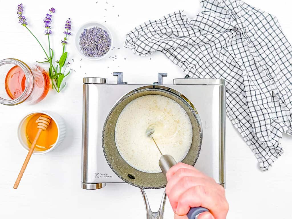 Milk being frothed using a milk frother in a pot on the stove.