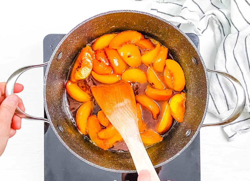 Peaches, sugar and water cooking in a large pot on the stove.