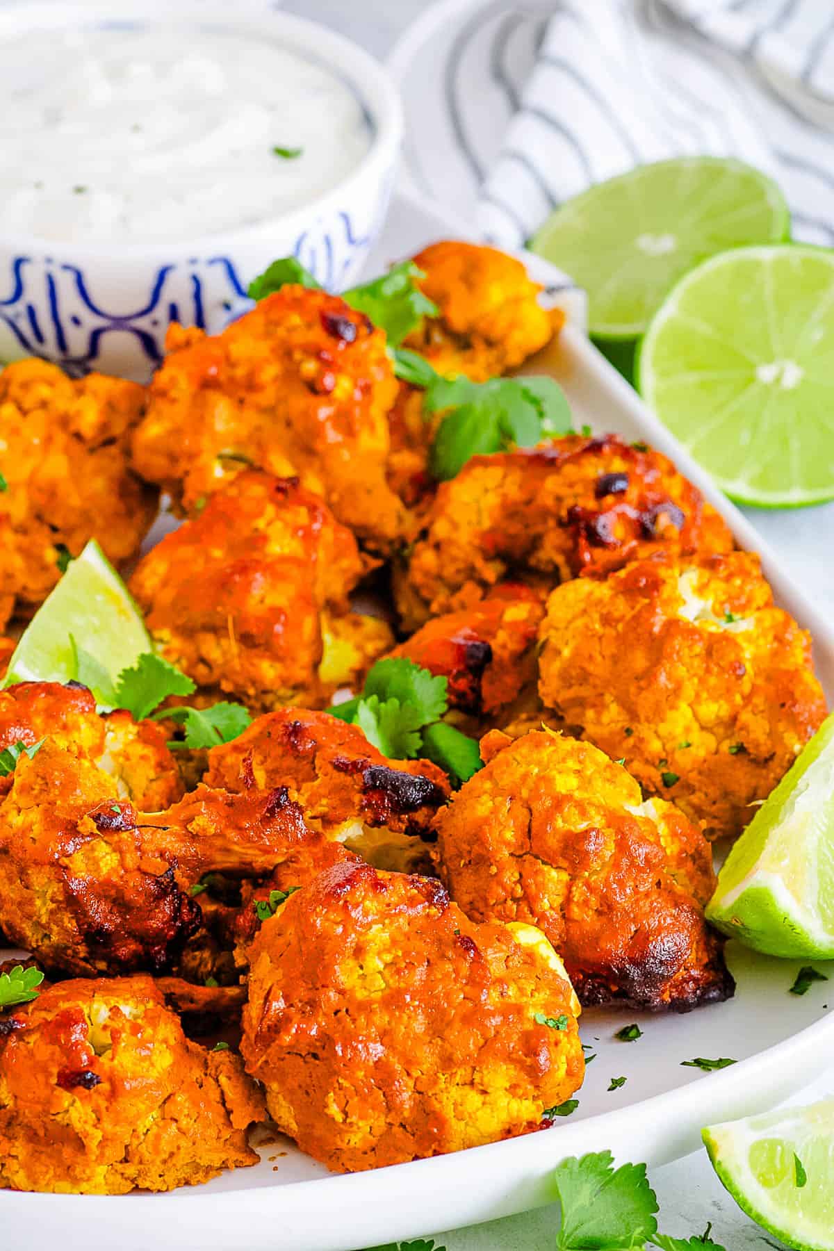 Healthy roasted tandoori cauliflower arranged on a white plate with a yogurt dipping sauce on the side.