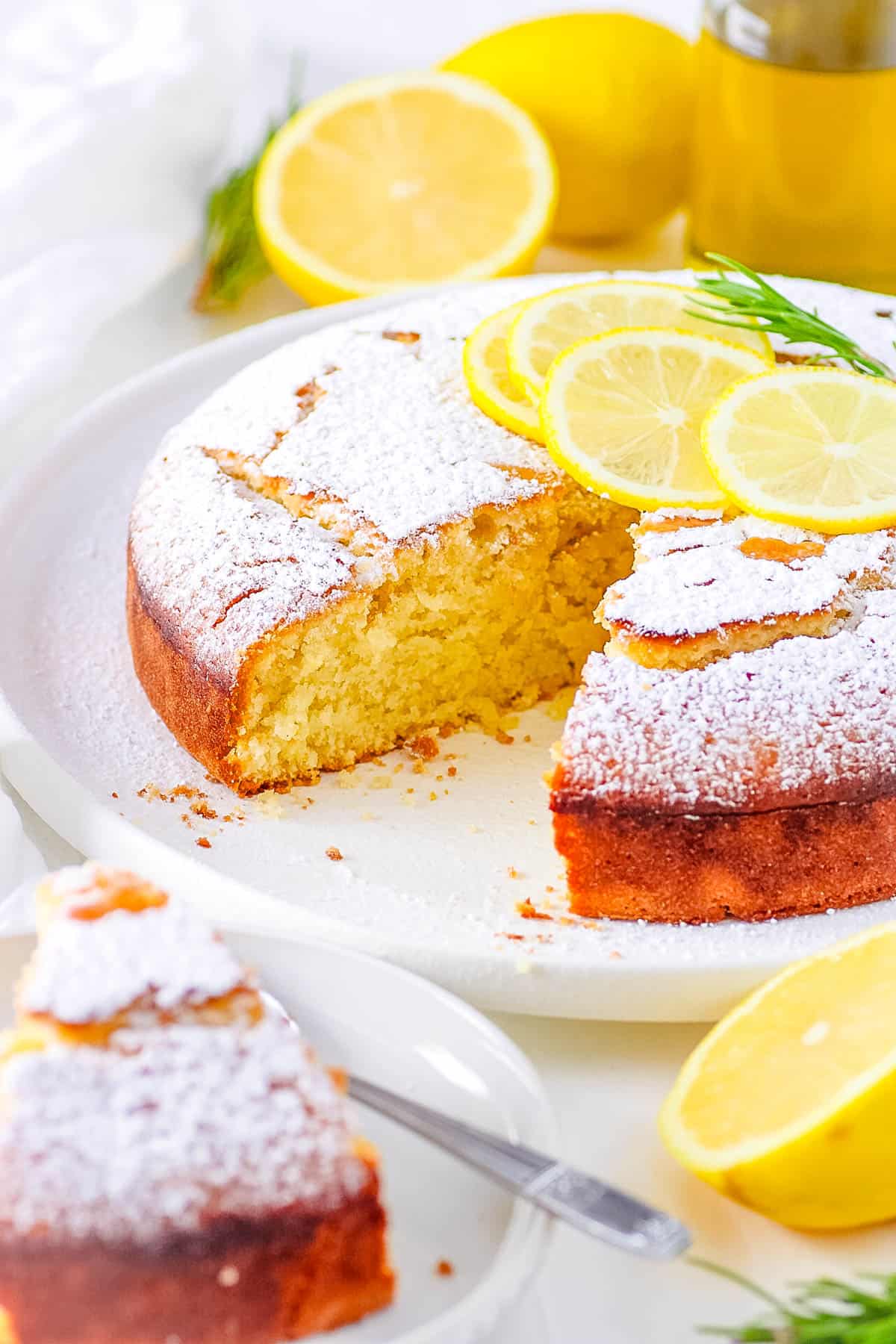 Easy lemon vegan olive oil cake on a cake stand with a piece cut out and served on a plate.