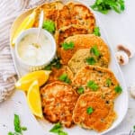 Easy mushroom fritters stacked on a white plate with dipping sauce on the side.