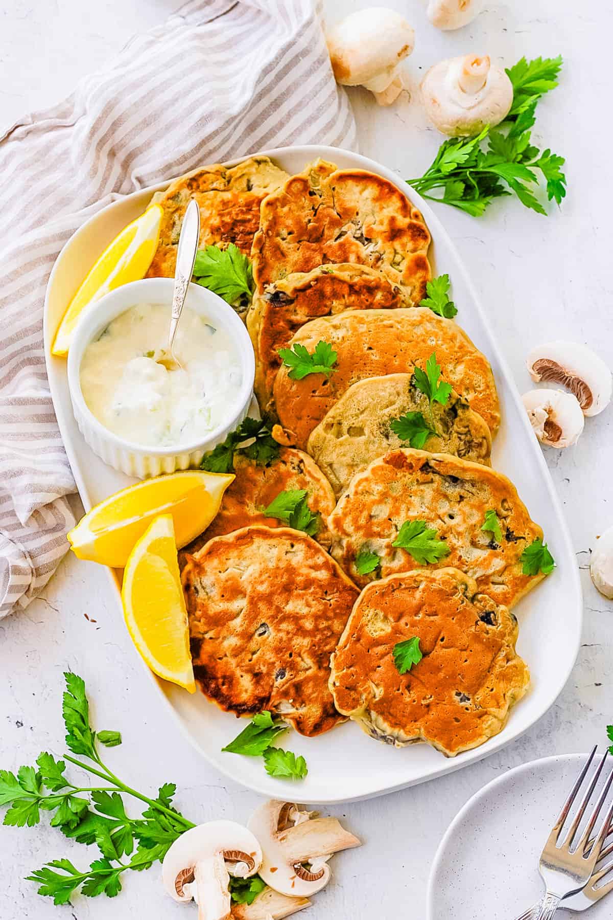 Easy mushroom fritters stacked on a white plate with dipping sauce on the side.