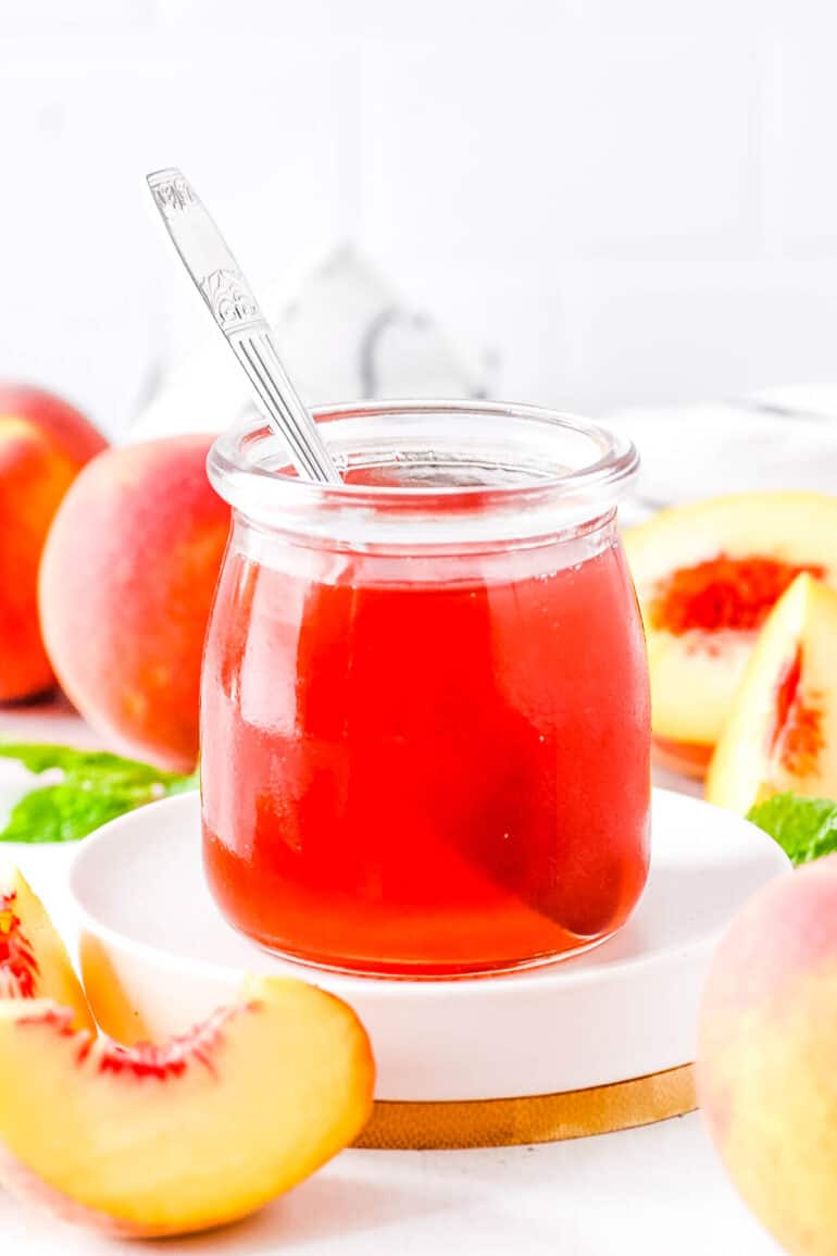 Peach syrup stored in a glass jar with a spoon inside the jar.