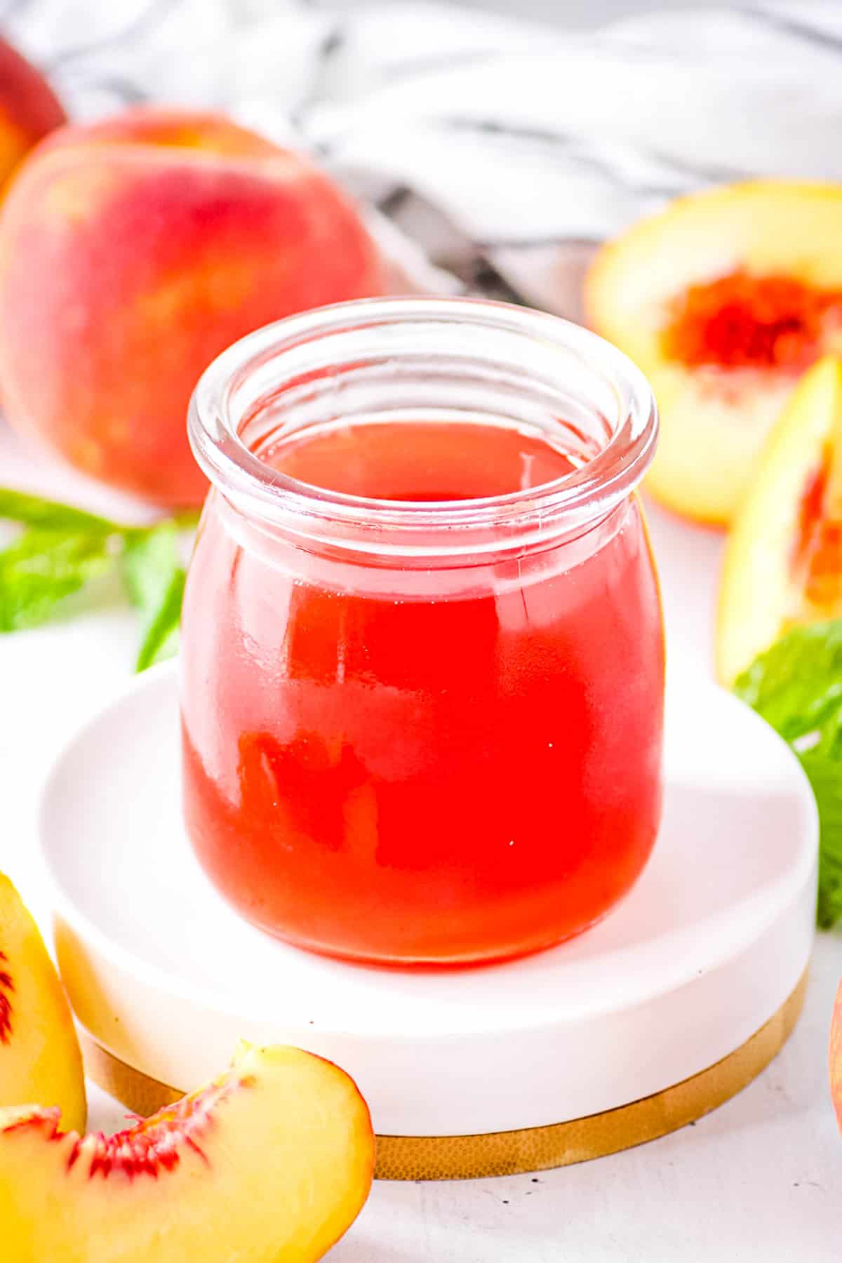 Easy peach simple syrup, stored in a glass jar, surrounded by fresh peach slices.