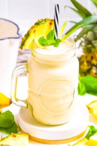 Pineapple and banana smoothie, served in a glass, garnished with a pineapple wedge and mint leaves.
