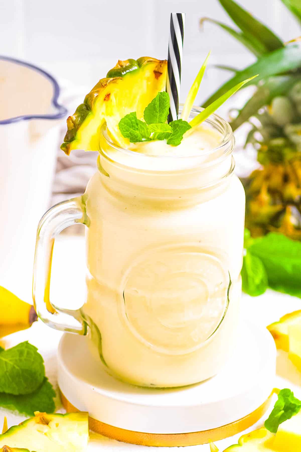 Pineapple and banana smoothie, served in a gl،, garnished with a pineapple wedge and mint leaves.