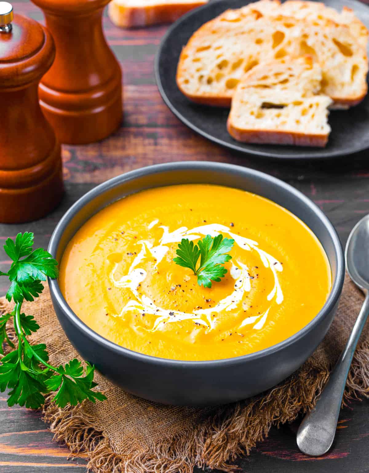 Pumpkin and sweet potato soup, served in a blue bowl, topped with fresh herbs and coconut cream.