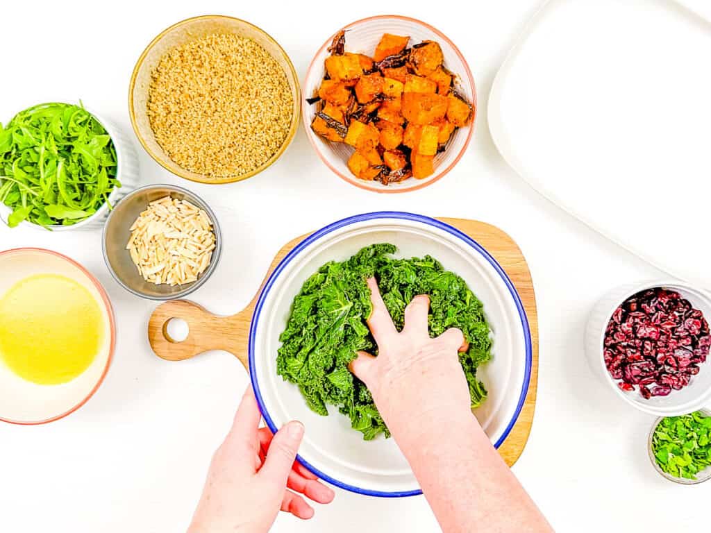 Kale being massaged in a mixing bowl.