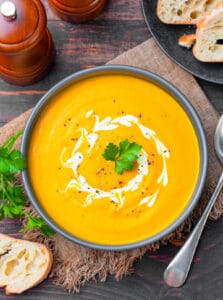 Pumpkin and sweet potato soup, served in a blue bowl, topped with fresh herbs and coconut cream.