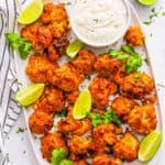 Tandoori cauliflower tikka arranged on a white plate with a yogurt dipping sauce on the side.