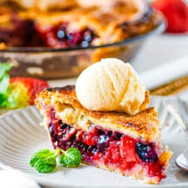 Slice of easy strawberry blueberry pie topped with ice cream with a whole pie in the background.