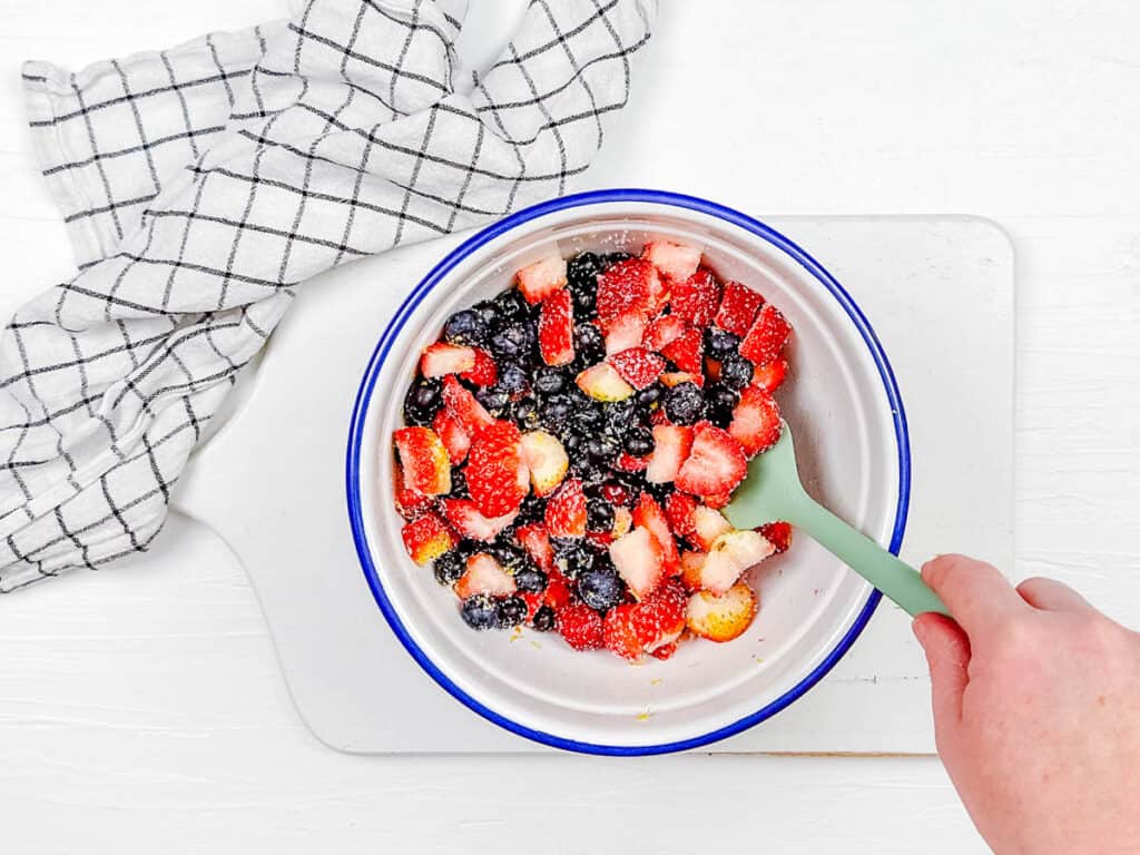 Berries mixed with sugar and corn starch in a mixing bowl.