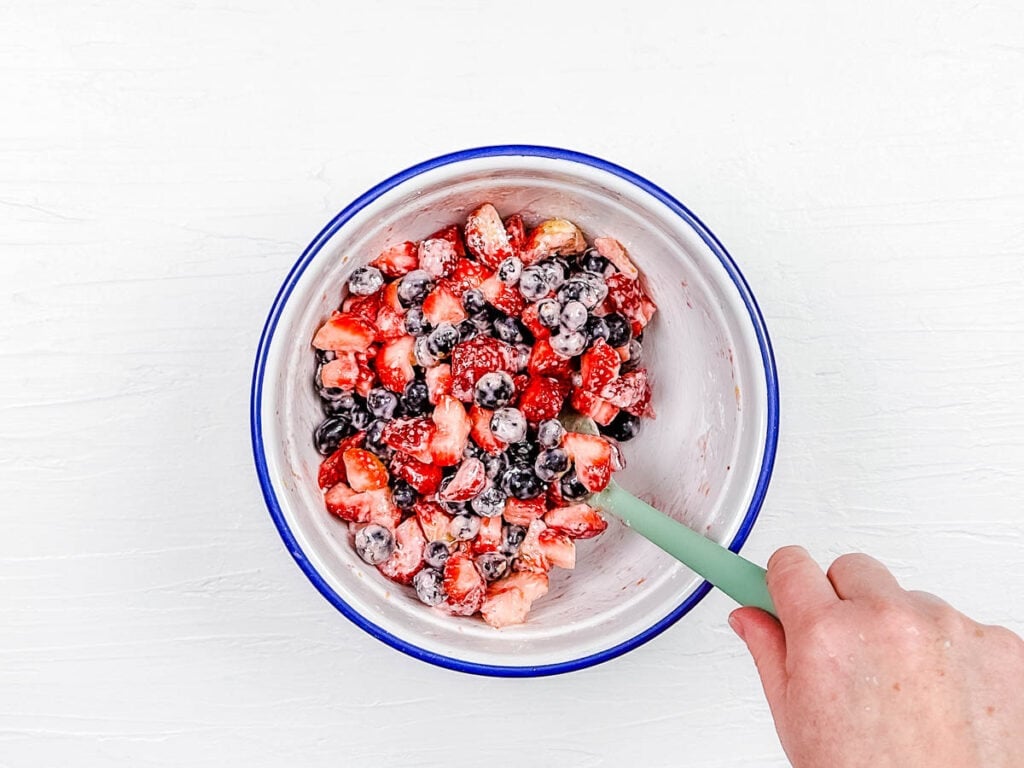 Fresh strawberries and blueberries mixed with sugar and corn starch in a mixing bowl.