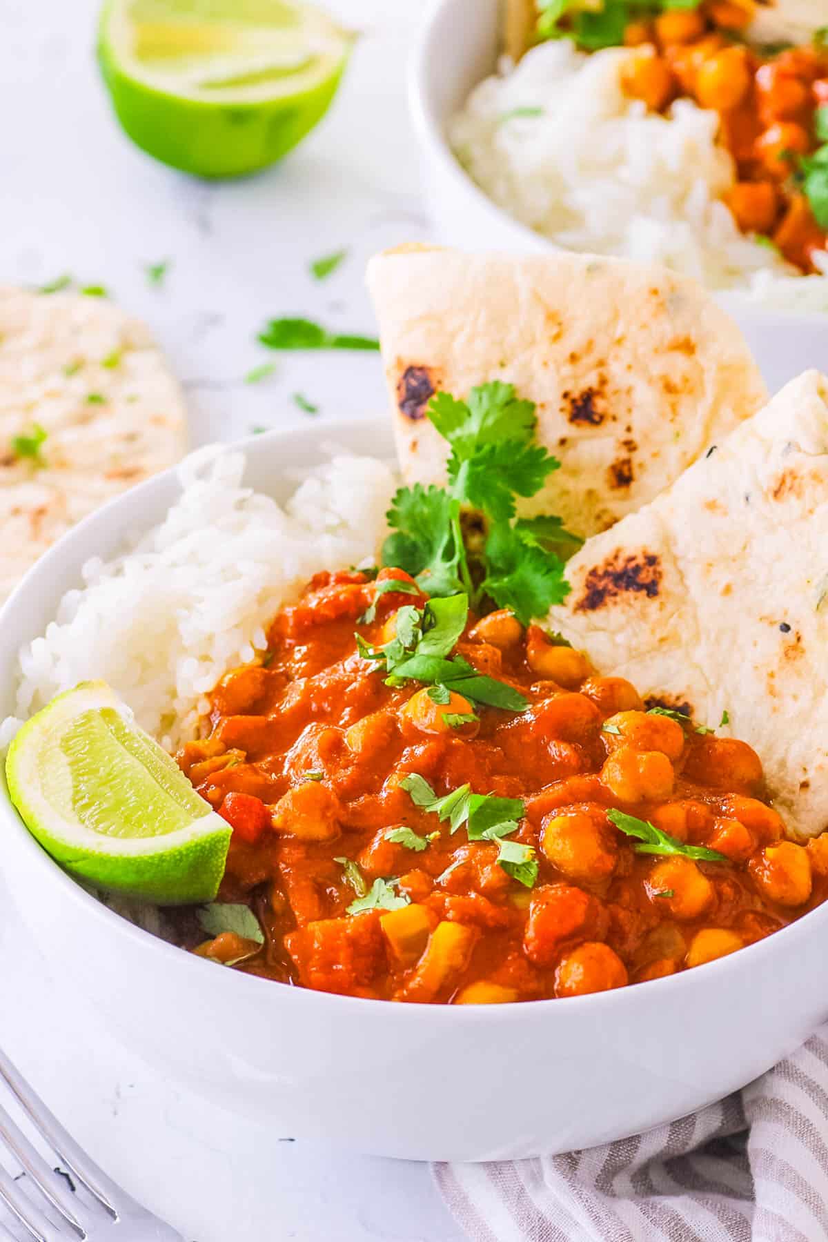 Easy chickpea tikka masala, served in a white bowl with naan and rice on the side, garnished with cilantro and lime.