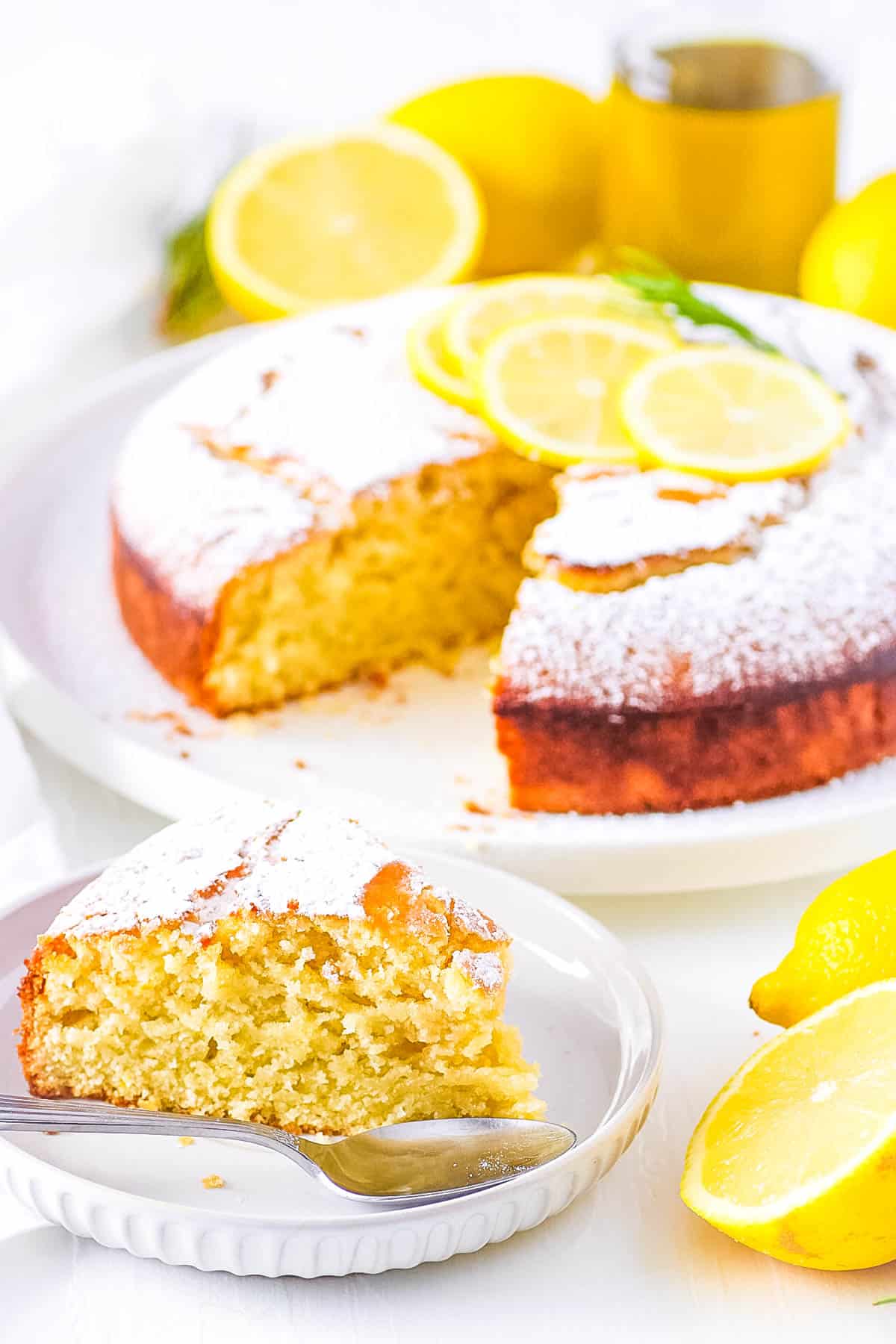 Lemon vegan olive oil cake on a cake stand with a piece cut out and served on a plate.
