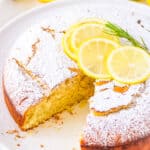 Lemon vegan olive oil cake on a cake stand, garnished with lemon slices and herbs.