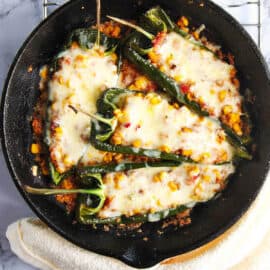 Vegetarian stuffed poblano peppers with melted cheese on top in a cast iron skillet.