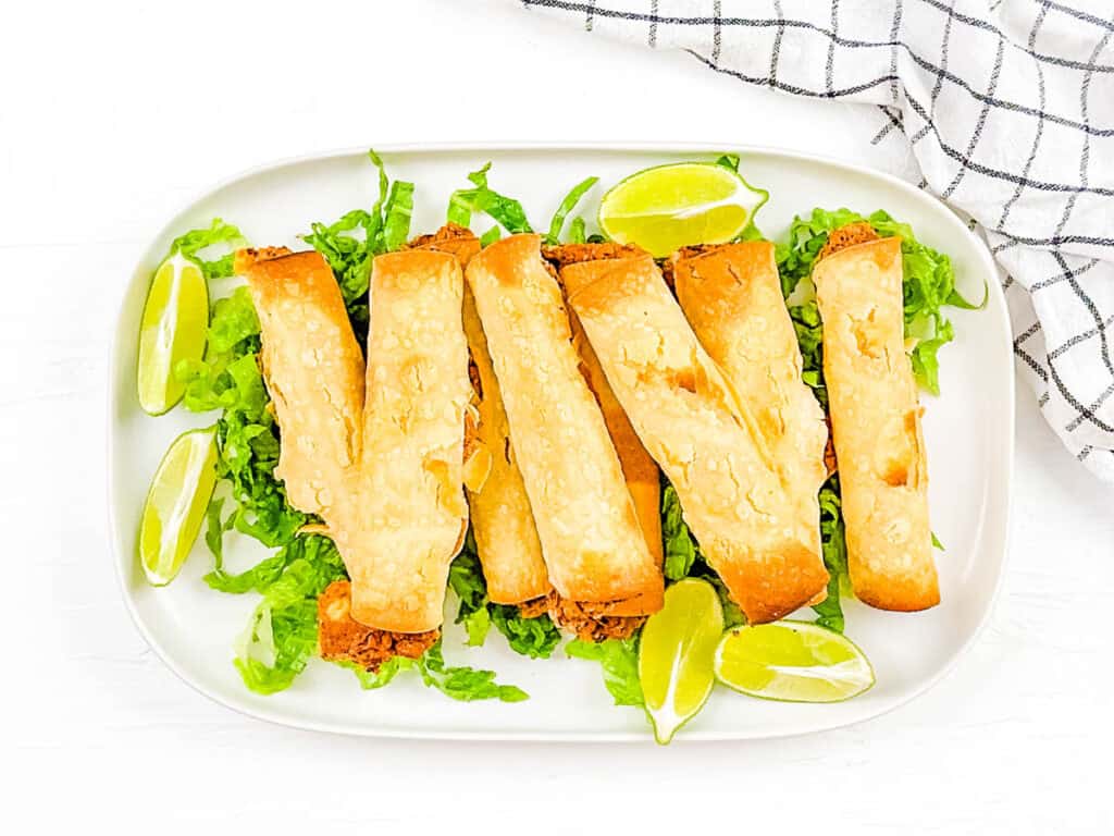 Corn tortillas rolled up and baked with vegan filling inside, served on a white plate.