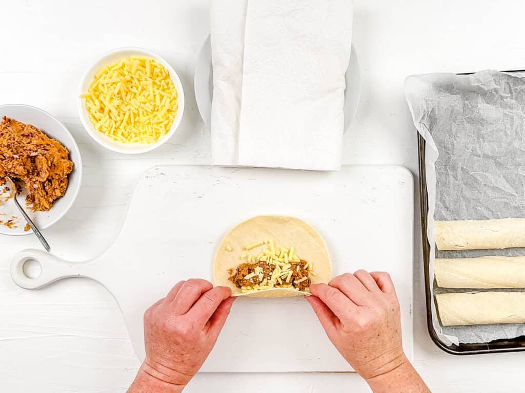 Corn tortilla with beans and vegan cheese inside, rolled up on a cutting board.